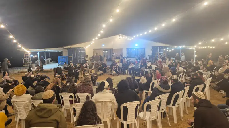 ערב של שיחה בחווה: קבוצה גדולה יושבת במעגל תחת שרשראות אור